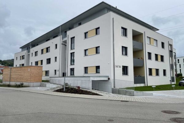 Modernes weißes Mehrfamilienhaus der FÖFA, Hausnummer 14/16, mit Balkonen und Holzverkleidung am Eingangsbereich