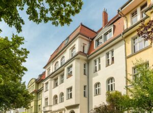 Historisches Altbau-Mehrfamilienhaus der FÖFA mit Stuckfassade, rotem Ziegeldach, Dachgauben und Erkern, umgeben von Bäumen